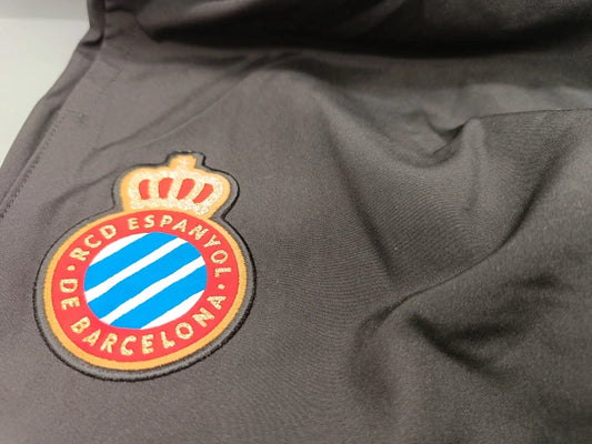 Detailaufnahme des Espanyol-Barcelona-Vereinswappens auf der dunkelgrauen Puma-Trainingshose