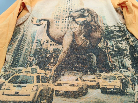 Detailaufnahme des großen T-Rex- und New-York-City-Motivs auf dem senfgelben Jungen-Langarmshirt in Größe 128