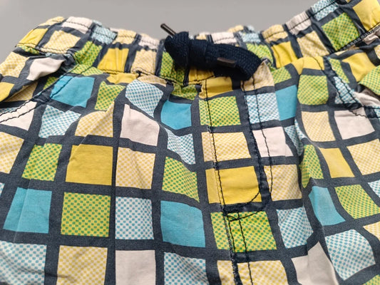 Detailaufnahme des bunten Karomusters in Gelb, Türkis, Grün, Creme und Dunkelblau auf den Jungen-Shorts in Größe 116