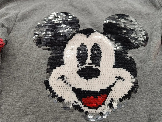 Detailaufnahme des glänzenden Mickey-Mouse-Motivs aus Wende-Pailletten auf dem grauen Mädchen-Sweatshirt in Größe 134