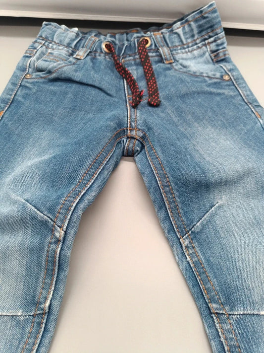 Detailaufnahme des elastischen Bundes, der Taschen und des rot-blauen Tunnelzugs der hellblauen Jungenjeans in Größe 98