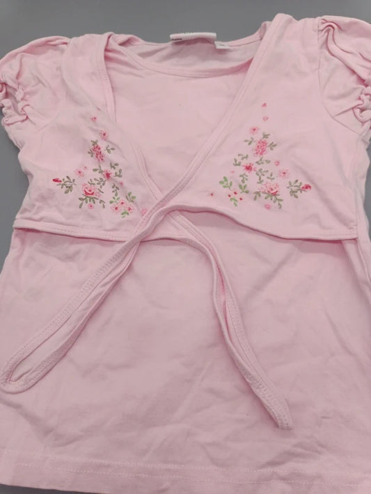 Detailaufnahme der floralen Stickerei und des Wickeldetails auf dem hellrosa Mädchen-Shirt