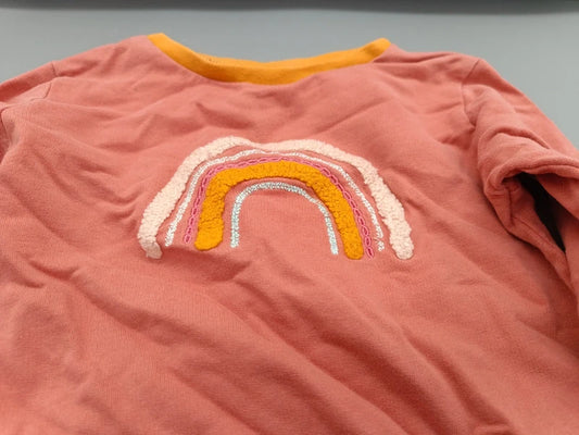 Detailaufnahme des bunten glitzernden Regenbogen-Aufnähers auf dem korallfarbenen Langarmshirt