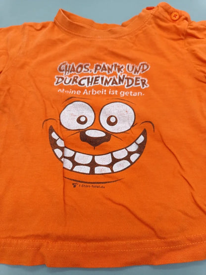 Detail des Aufdrucks mit grinsendem Gesicht und Spruch auf dem orangefarbenen T-Shirt