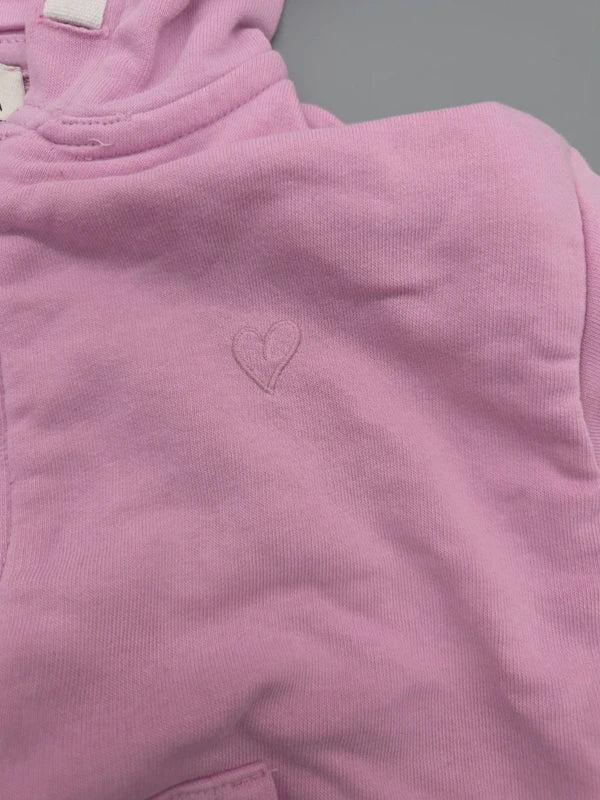 Kleines Herzdetail auf der Brust der roséfarbenen Sweatjacke